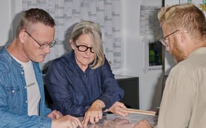 Three colleagues reviewing project plans and documents together during a collaborative office meeting.